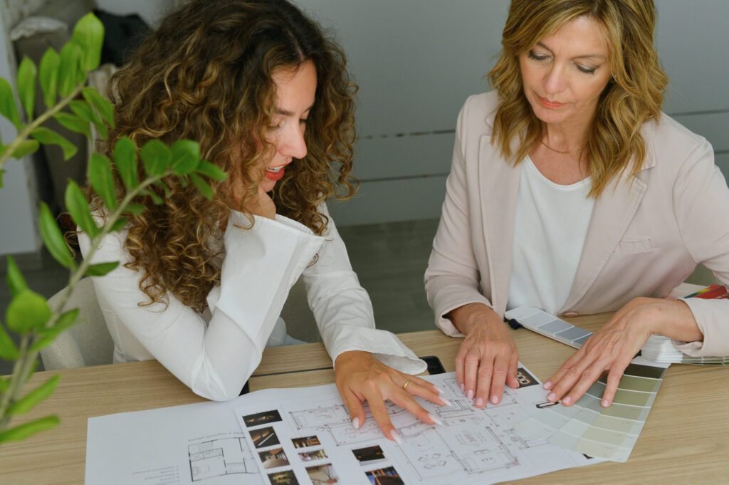 Proyecto Transformador | Coaching de Neurointeriorismo Dos mujeres revisando planos y paletas de colores en una mesa de interiorismo.