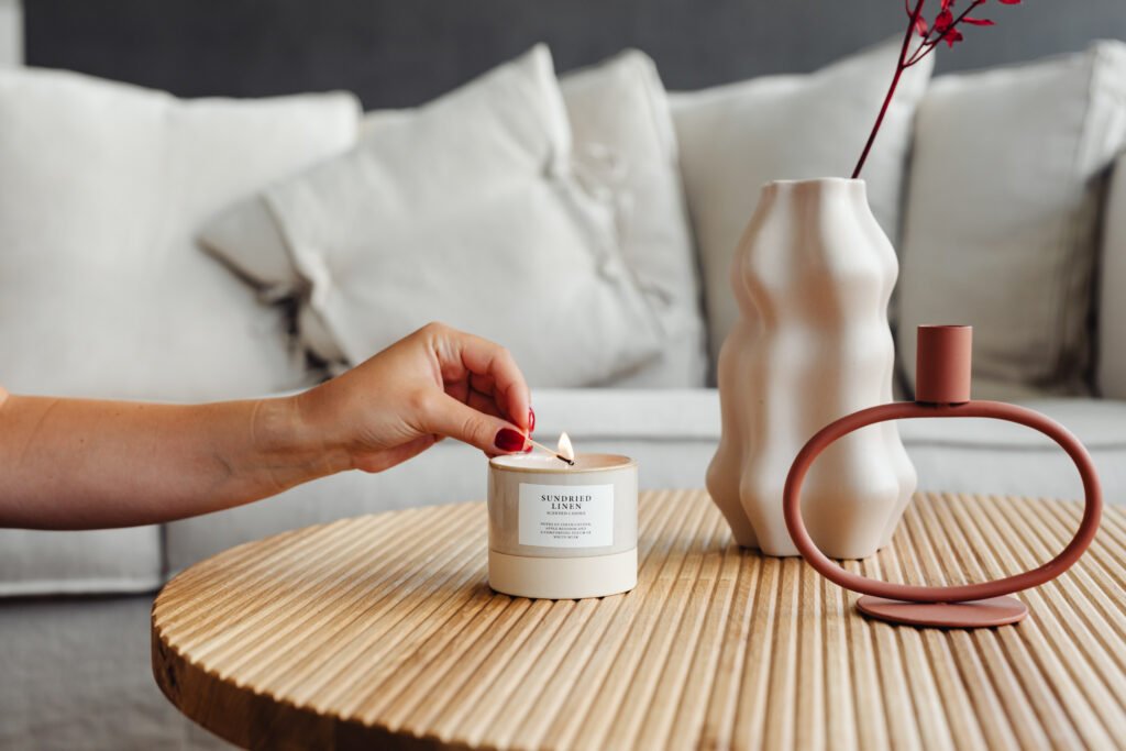 Mano encendiendo vela aromática sobre mesa de madera con jarrón beige