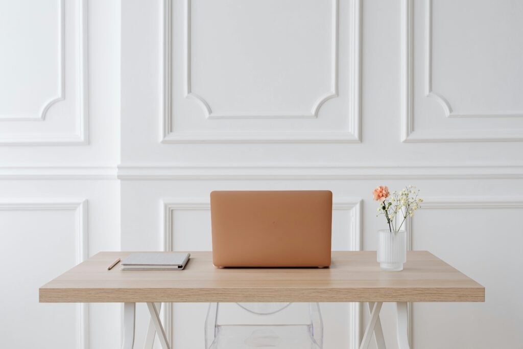 Asesoría de interiorismo online | SENTIER Escritorio minimalista con portátil, libreta y flor en jarrón blanco.