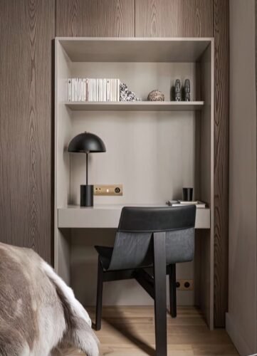 Escritorio empotrado con silla negra y lámpara de lectura en dormitorio neutro.