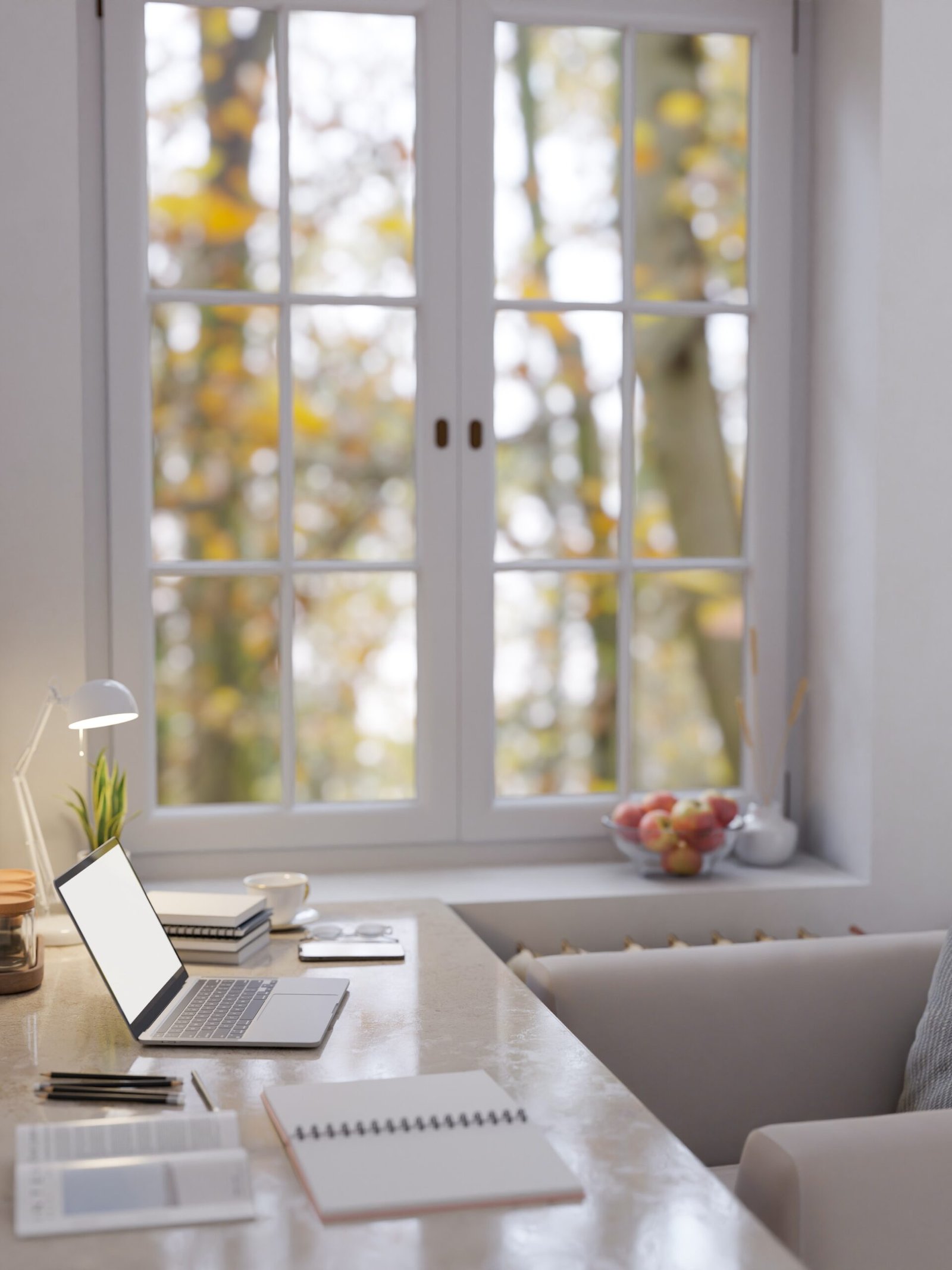Espacio de trabajo luminoso con vistas naturales Escritorio junto a ventana con portátil, cuadernos y luz de otoño al fondo.