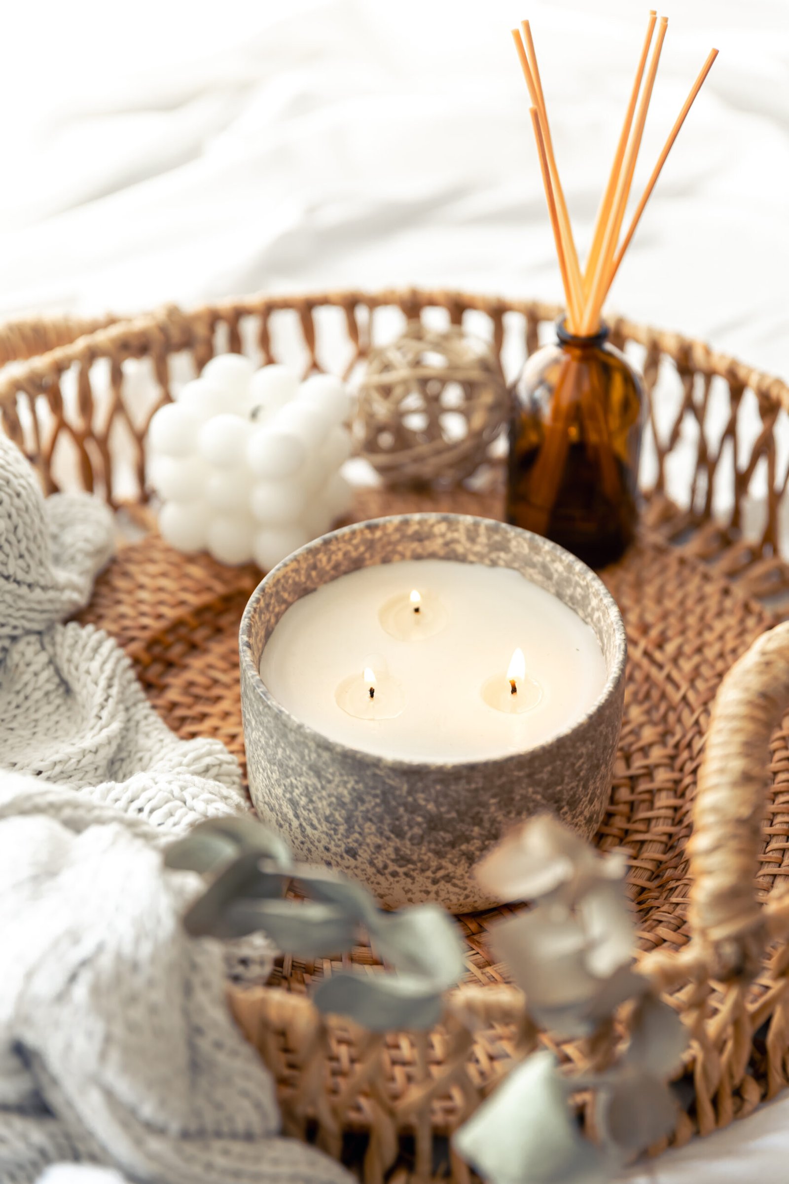 Cesta de mimbre con vela encendida, difusor de varillas y manta gris