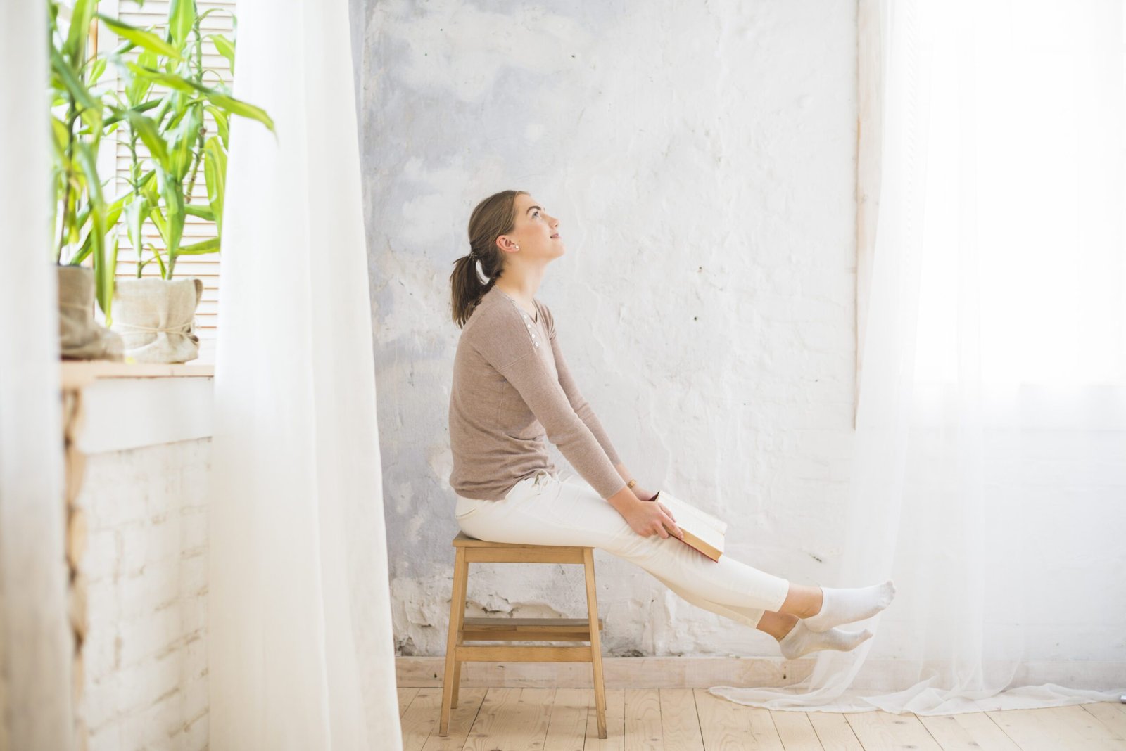 Dona asseguda amb un llibre en un espai lluminós i natural, simbolitzant un moment de reflexió sobre la pròpia llar.