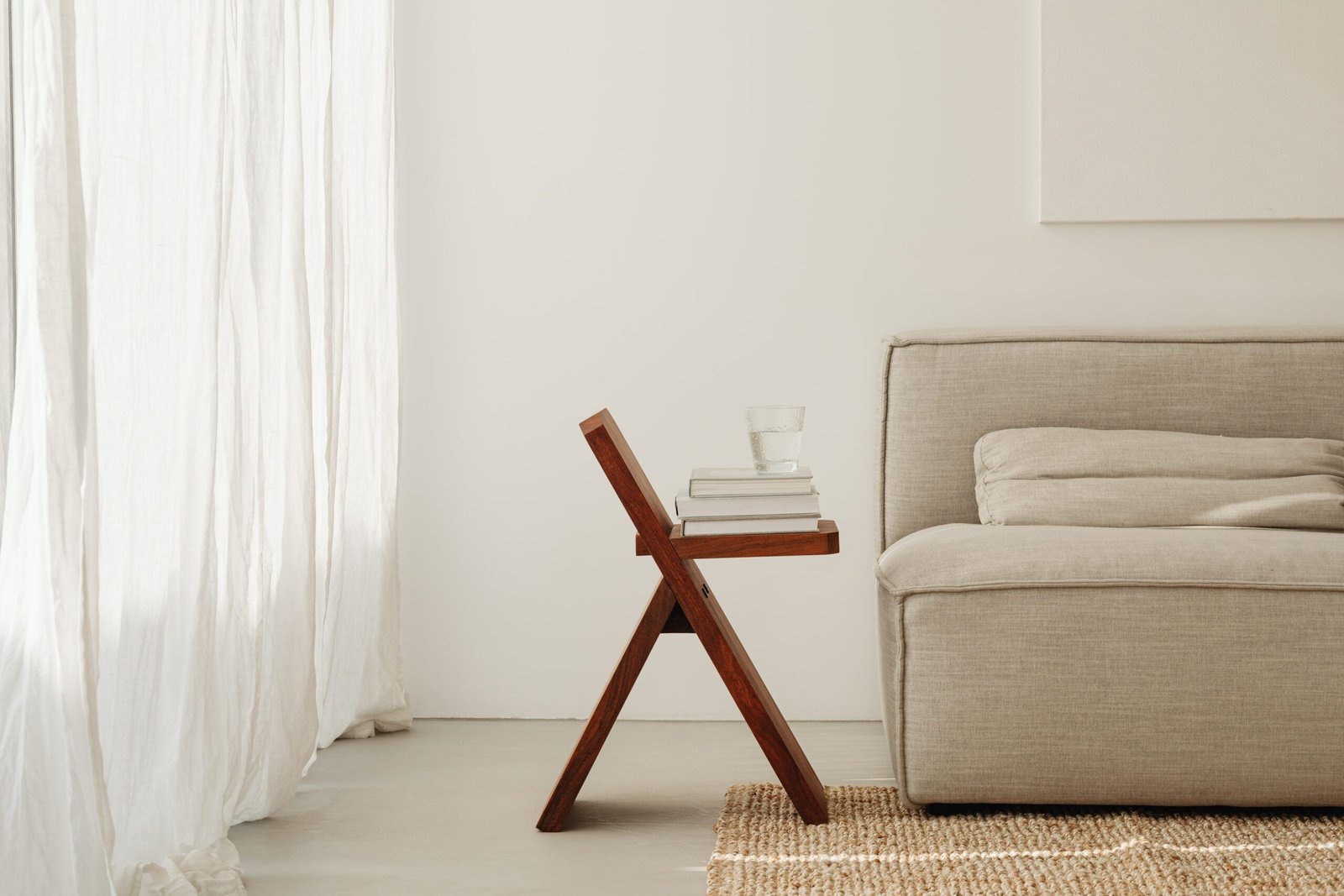 Taburete de madera con libros y un vaso de agua junto al sofá en un ambiente tranquilo