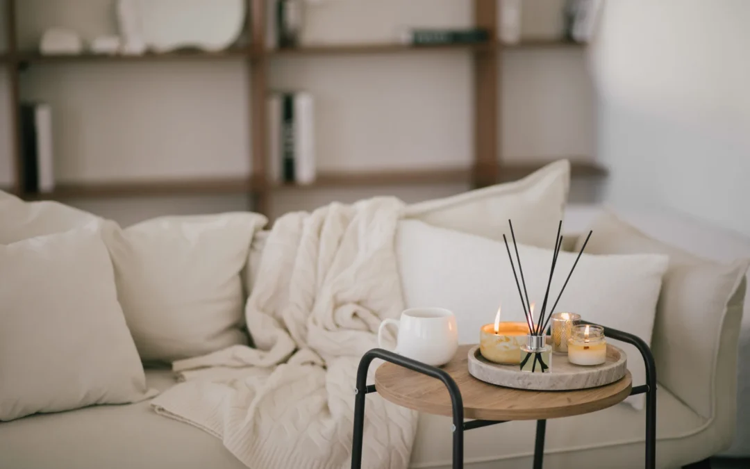 Sofà beix amb manta i difusor aromàtic sobre una tauleta auxiliar en un saló acollidor